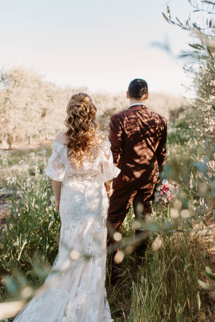 Bride and groom walking through flowered meadow for wedding photos